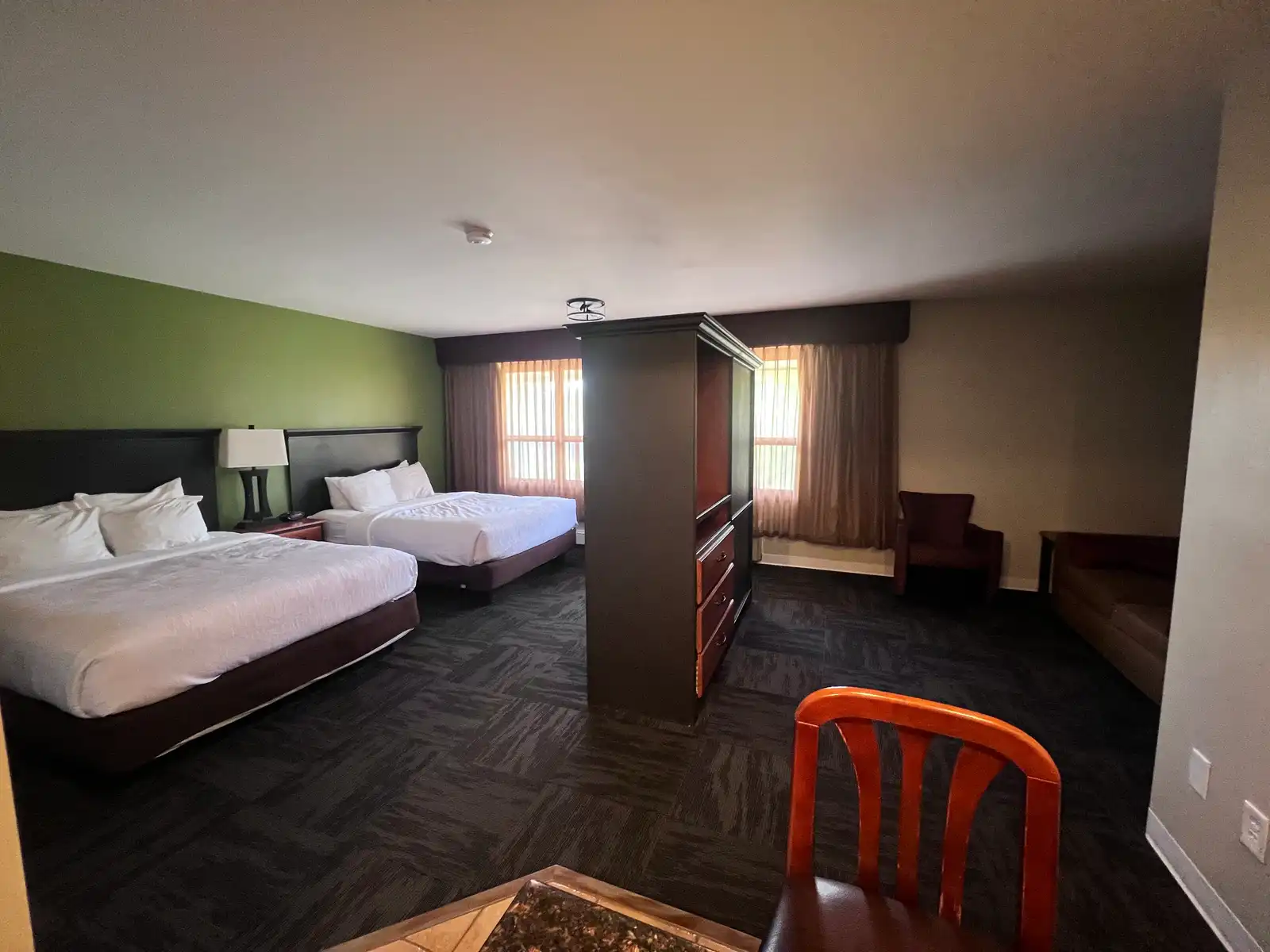 A Family Suite at The DL Hotel, with two queen beds on one side of a divider and a sitting area with an armchair and table on the other